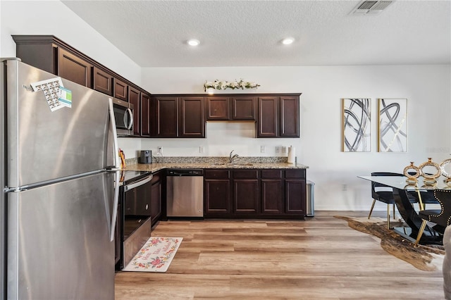 kitchen featuring visible vents, dark brown cabinetry, light wood-type flooring, light stone counters, and appliances with stainless steel finishes