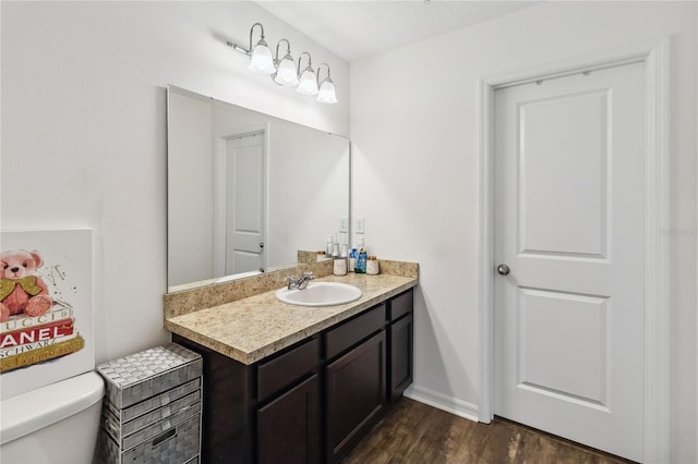 bathroom with vanity, toilet, wood finished floors, and baseboards