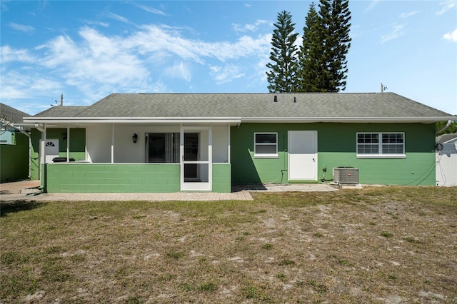 rear view of property featuring a shingled roof, central air condition unit, concrete block siding, a yard, and a sunroom