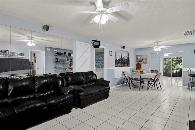 living area featuring light tile patterned floors, visible vents, a textured ceiling, and a ceiling fan