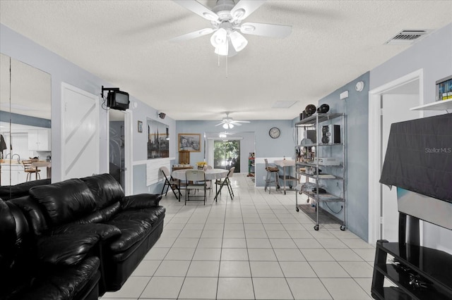 living area with light tile patterned flooring, a ceiling fan, visible vents, and a textured ceiling