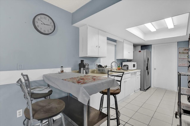 kitchen with light tile patterned floors, white microwave, light countertops, white cabinets, and stainless steel fridge