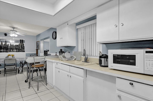 kitchen featuring a sink, white microwave, white cabinets, and light countertops