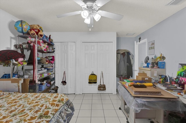 bedroom with visible vents, two closets, ceiling fan, light tile patterned floors, and a textured ceiling