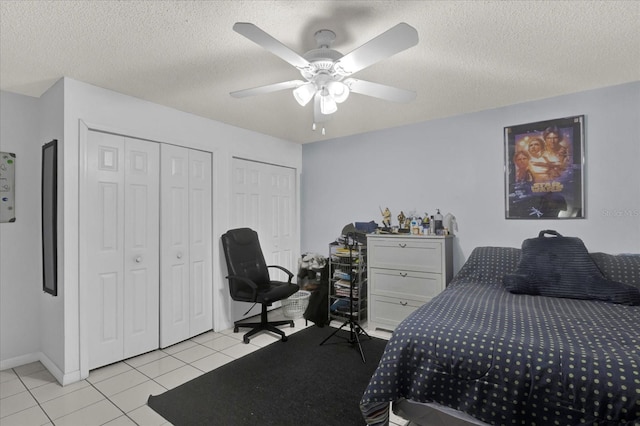 bedroom featuring baseboards, ceiling fan, multiple closets, light tile patterned floors, and a textured ceiling