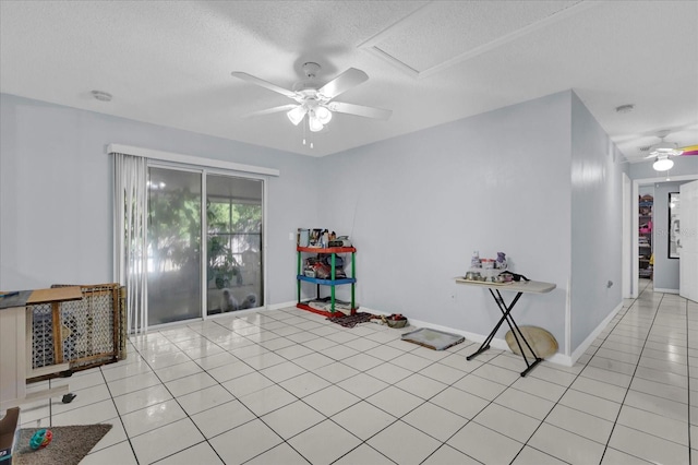 interior space with light tile patterned floors, a ceiling fan, baseboards, and a textured ceiling