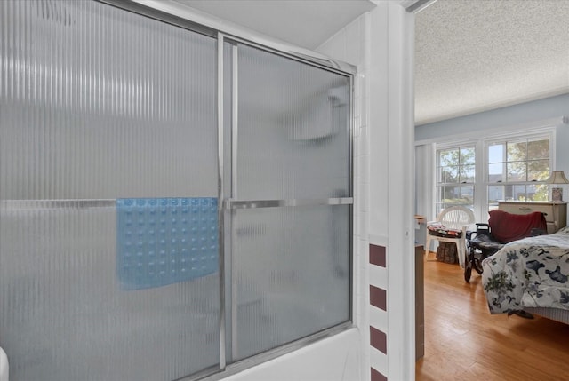 bathroom with enclosed tub / shower combo, wood finished floors, and a textured ceiling