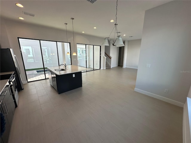 kitchen featuring visible vents, a kitchen island with sink, a sink, open floor plan, and light countertops