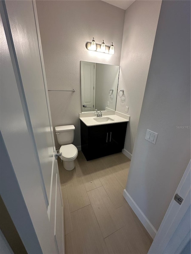 half bathroom featuring vanity, toilet, baseboards, and wood tiled floor