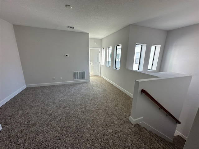 unfurnished room featuring baseboards, visible vents, a textured ceiling, and carpet