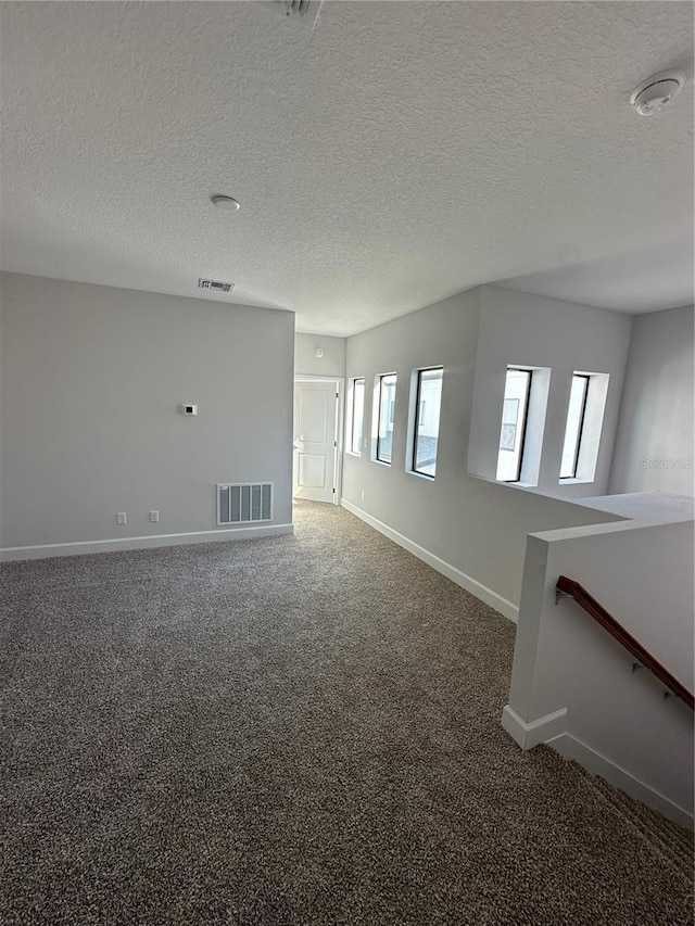 carpeted spare room featuring baseboards, visible vents, and a textured ceiling