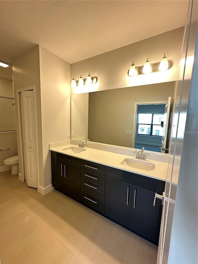 full bathroom with a textured ceiling, double vanity, toilet, and a sink