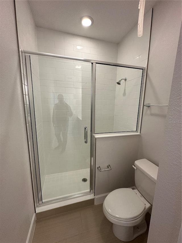 bathroom featuring a stall shower, toilet, and baseboards