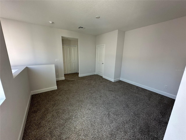 unfurnished bedroom featuring baseboards, visible vents, dark carpet, and a textured ceiling