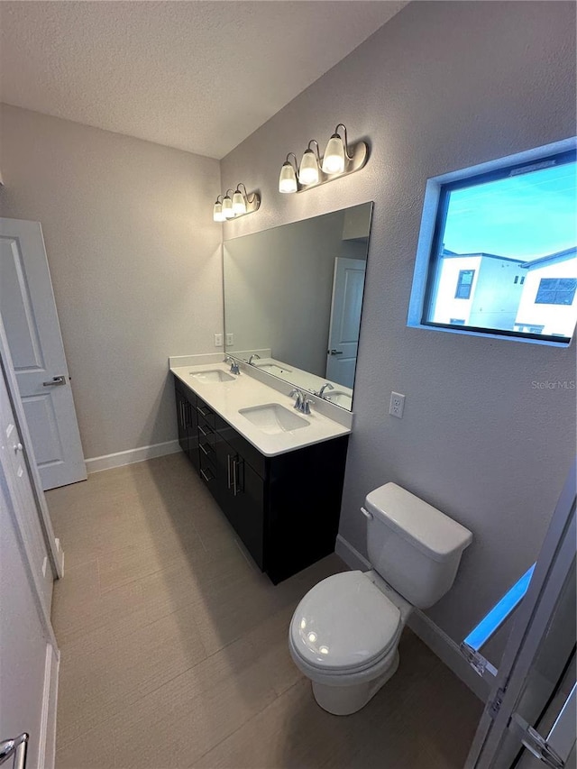 bathroom with double vanity, toilet, baseboards, and a sink