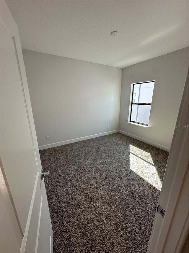 unfurnished room featuring baseboards and dark colored carpet