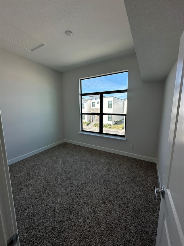 spare room featuring dark colored carpet, baseboards, and attic access