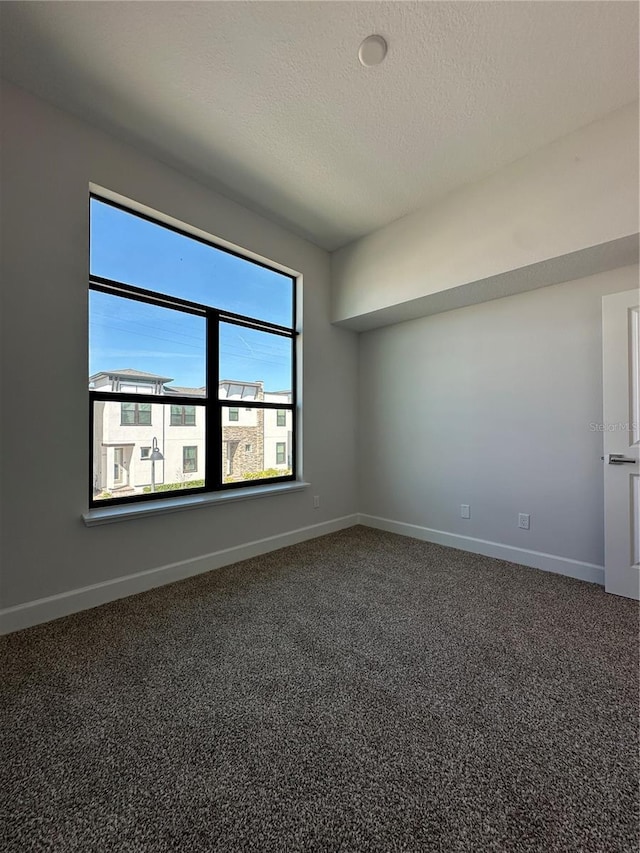 unfurnished room with dark carpet, a textured ceiling, and baseboards