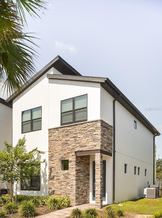 view of front of house featuring stone siding, stucco siding, and central AC unit