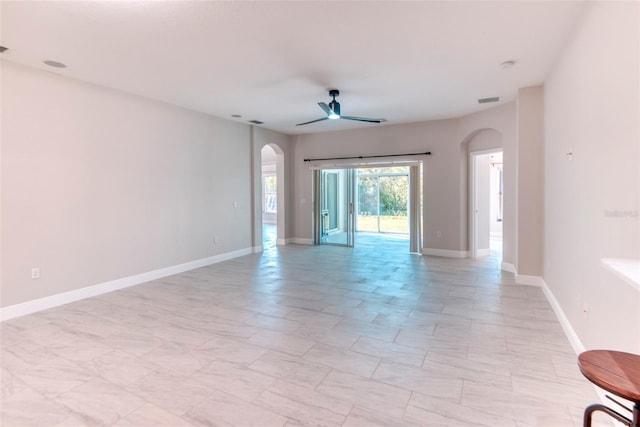 empty room featuring arched walkways, visible vents, baseboards, and ceiling fan