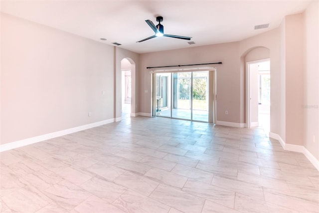 empty room featuring a ceiling fan, visible vents, arched walkways, and baseboards