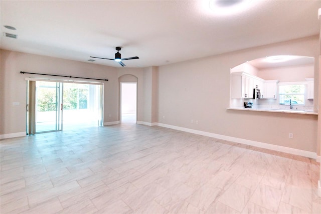 unfurnished living room featuring arched walkways, visible vents, plenty of natural light, and ceiling fan