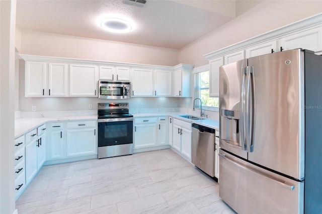 kitchen featuring light stone counters, appliances with stainless steel finishes, white cabinetry, and a sink