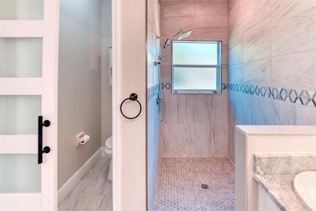 full bathroom with baseboards, tiled shower, toilet, and vanity