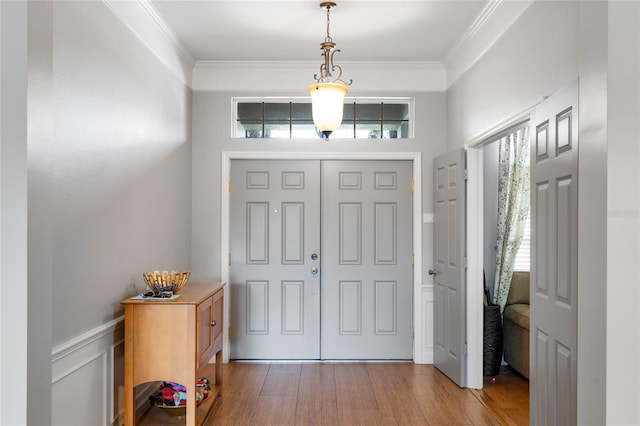 entryway with wainscoting, wood finished floors, and ornamental molding