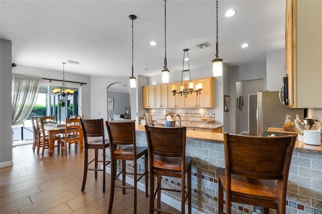 kitchen featuring backsplash, light brown cabinets, a chandelier, light countertops, and arched walkways