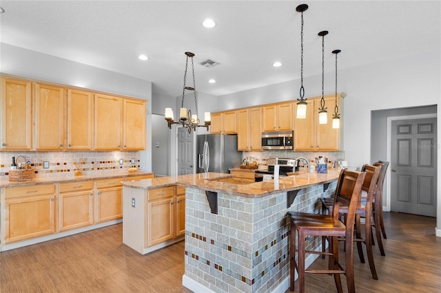 kitchen with light wood finished floors, light brown cabinets, a chandelier, a kitchen bar, and appliances with stainless steel finishes