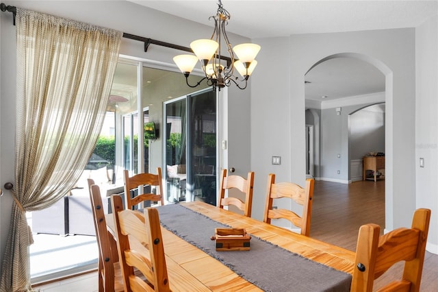 dining room with baseboards, wood finished floors, arched walkways, and a chandelier