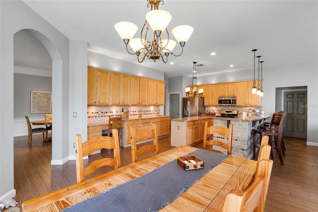 dining space with an inviting chandelier, wood finished floors, arched walkways, and baseboards