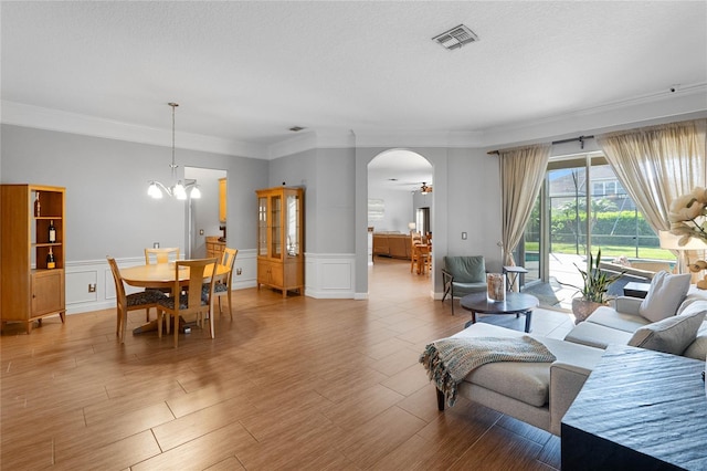 living area featuring light wood-type flooring, visible vents, a notable chandelier, ornamental molding, and arched walkways