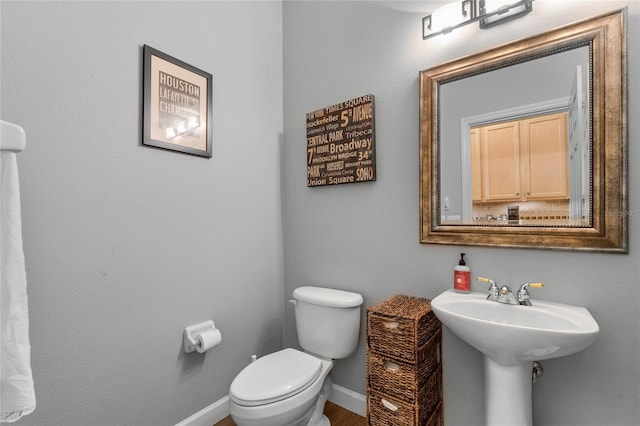 half bathroom featuring toilet, baseboards, and a sink