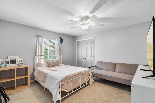 bedroom with a ceiling fan, light colored carpet, a closet, and a textured ceiling