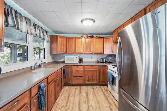 kitchen featuring brown cabinets, white appliances, light wood-style floors, and a sink