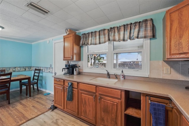 kitchen featuring light wood finished floors, visible vents, crown molding, brown cabinetry, and a sink