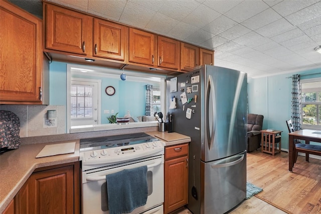 kitchen with white range with electric cooktop, brown cabinets, freestanding refrigerator, and light wood-style floors