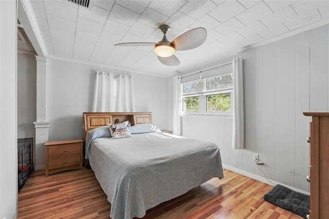 bedroom with decorative columns, a ceiling fan, wood finished floors, and crown molding