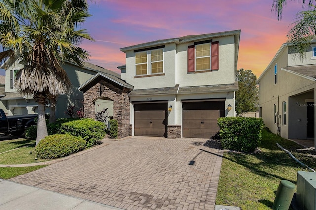 view of front of house with decorative driveway, stone siding, an attached garage, and stucco siding