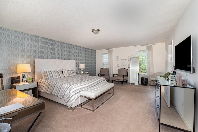 bedroom featuring light colored carpet, a textured ceiling, an accent wall, and wallpapered walls