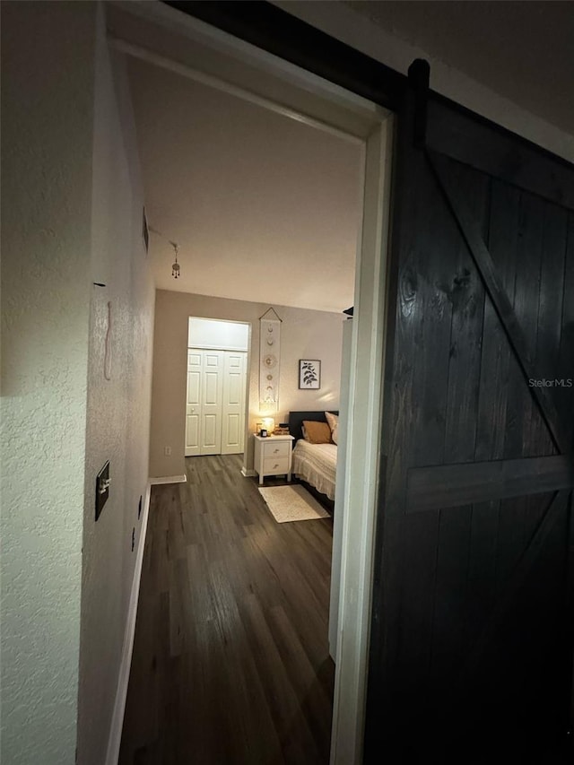 hallway with dark wood finished floors, a barn door, baseboards, and a textured wall