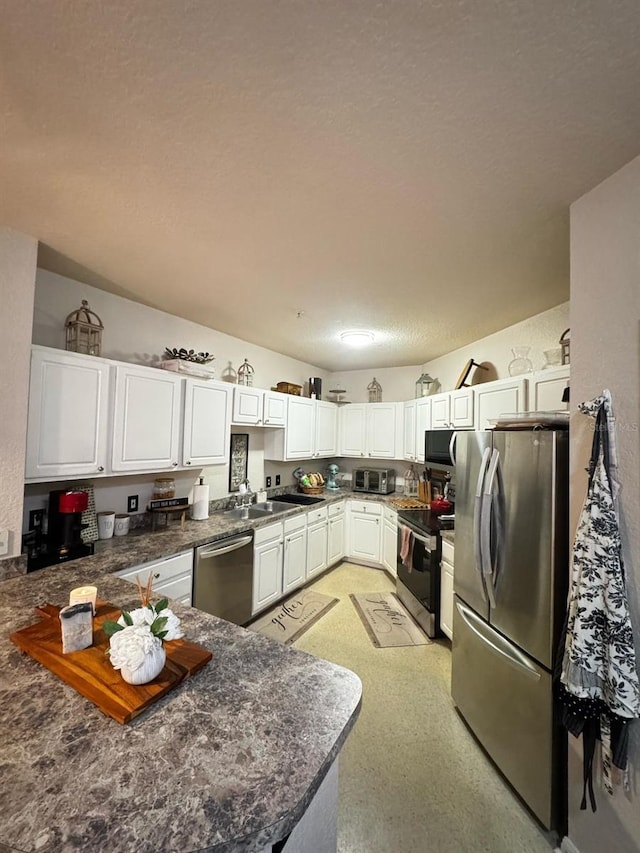 kitchen featuring a sink, dark countertops, white cabinetry, appliances with stainless steel finishes, and a peninsula