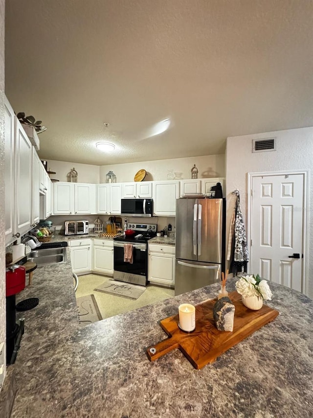 kitchen featuring visible vents, a sink, stainless steel appliances, dark stone counters, and white cabinets