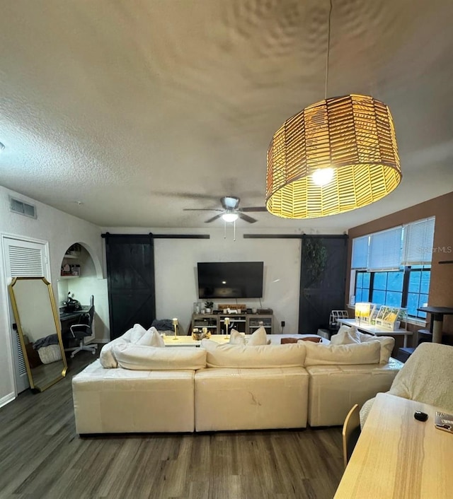 living area with visible vents, a textured ceiling, wood finished floors, arched walkways, and ceiling fan