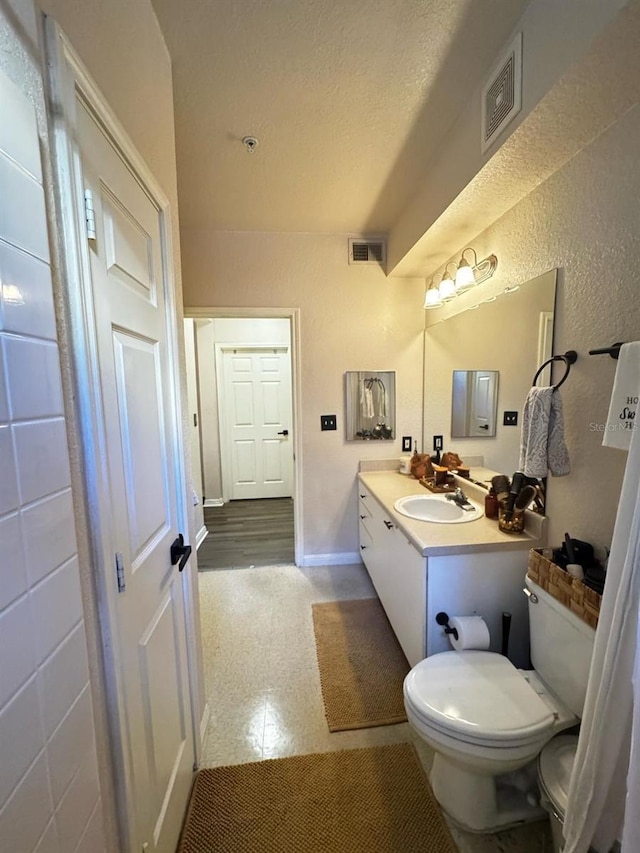 bathroom with visible vents, toilet, vanity, and a textured ceiling