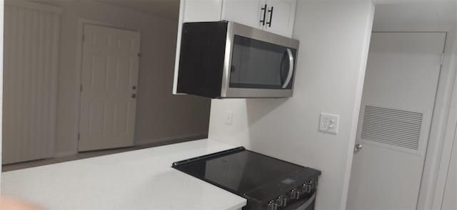 kitchen featuring white cabinetry, stainless steel microwave, black range with electric stovetop, and light countertops