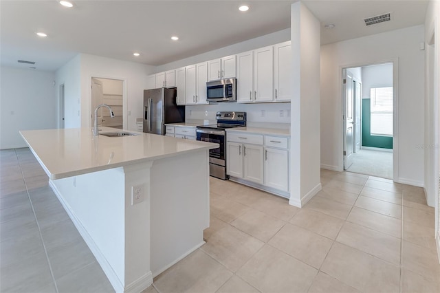 kitchen featuring visible vents, a kitchen island with sink, a sink, appliances with stainless steel finishes, and white cabinets