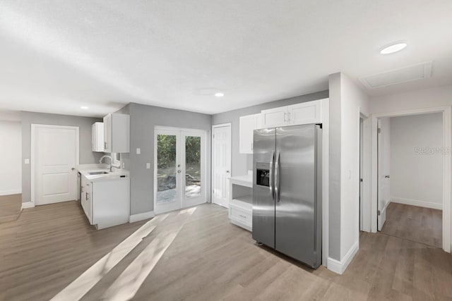 kitchen with a sink, white cabinetry, stainless steel fridge, light wood-style floors, and light countertops